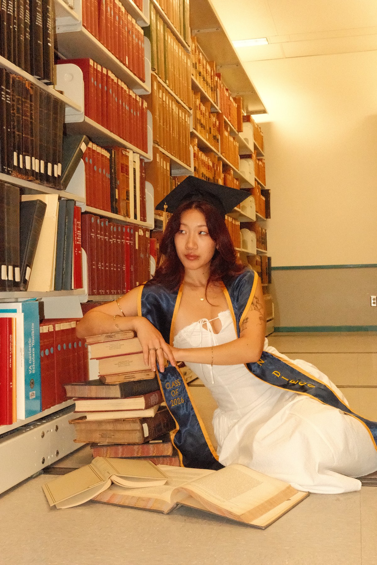 Serina Li in a graduation cap and sash, seated among library books